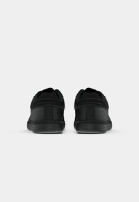 Black sneakers with a smooth synthetic upper, padded collar, and textured heel. Features contrasting stitching and a rubber sole.