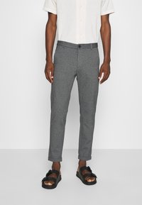 Pantalons gris fuselés en tissu texturé, dotés d'une fermeture à bouton, de poches latérales et de poignets retroussés, associés à des sandales noires.