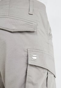 Grå cargo bukser med kla flap lomme og metalllogo aksent. Stoffet er slitesterkt med synlige sømmer og et avslappet passform-design.