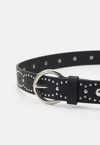Μαύρη δερμάτινη ζώνη με ασημένιες καρφίτσες και κυκλική μεταλλική αγκράφα. Διαθέτει ομοιόμορφα κατανεμημένες τρύπες και λεία υφή. Ανθεκτικός και κομψός σχεδιασμός.