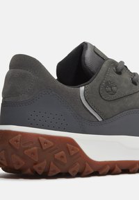 Zapatilla de ante gris con suela de goma, que presenta un lateral texturizado gris, perforaciones para transpirabilidad y un acento del logo.