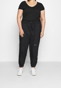 Svart kortärmad topp och svarta joggarbyxor med elastiska muddar. Byxorna har sidofickor och en liten vit Nike swoosh-logotyp. Vita skor.