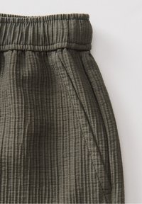 Ceinture élastique d’un pantalon en tissu côtelé gris foncé avec couture latérale visible et ouverture de poche sur un fond clair.
