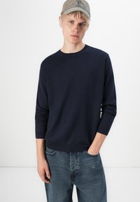 Navy knit sweater with round neck and ribbed cuffs, paired with light blue denim jeans. Smooth texture; minimal detailing on fabric.
