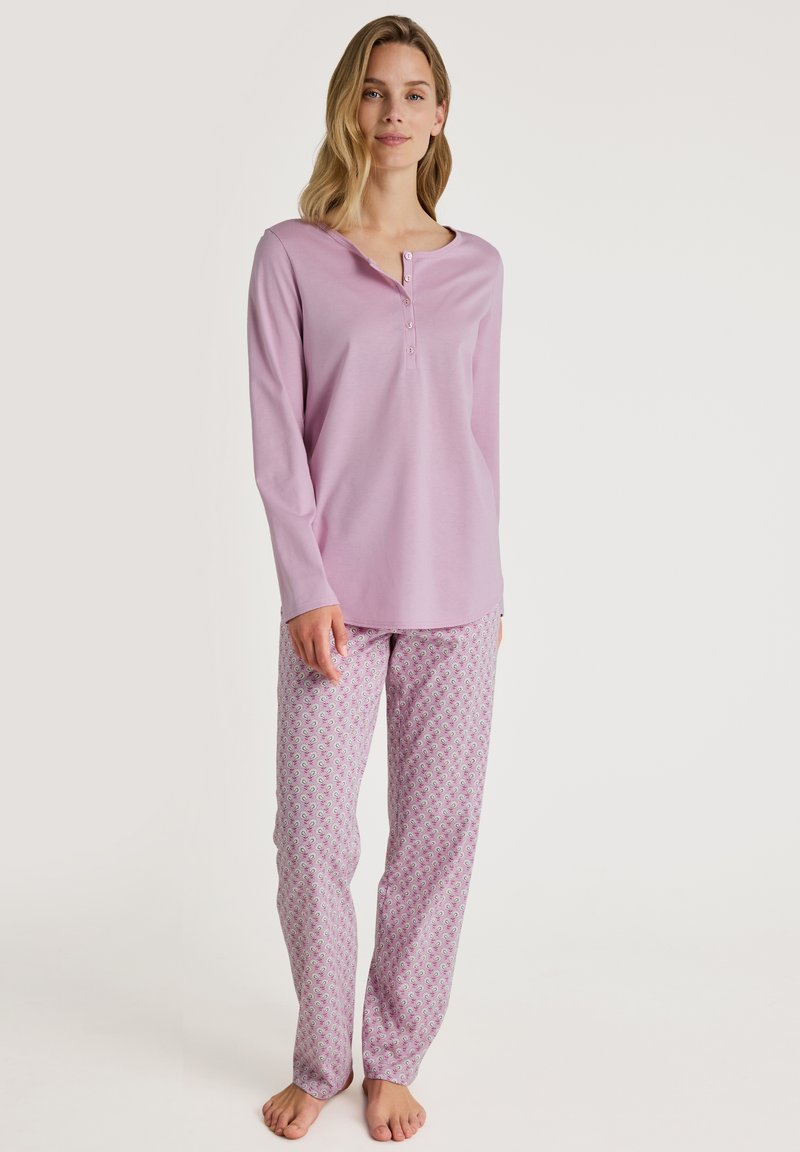 Lange mouwen lichtpaarse pyjama top met een henley halslijn; gedragen met een pyjamabroek met een patroon van roze en witte bloemen.