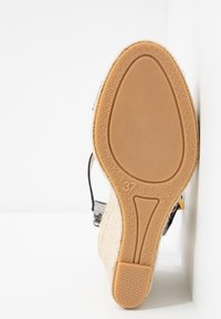 Semelle d'une sandale compensée beige indiquant la taille 37, avec une semelle en caoutchouc texturée et des côtés en tissu tissé beige.