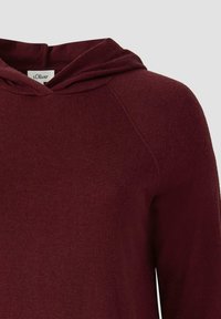 Burgundowy hoodie o luźnym kroju, z kapturem na sznurku, miękką teksturą i rękawami raglanowymi. Materiał wydaje się lekki i przytulny.