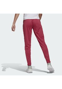 Czerwone spodnie sportowe o dopasowanym kroju, zwężanych nogawkach i bocznych kieszeniach; wykonane z gładkiego, lekkiego materiału; noszone z białymi trampkami.