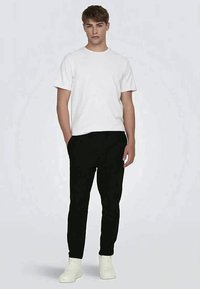 White cotton T-shirt paired with black tapered joggers and white sneakers. The joggers feature side pockets and a smooth texture.