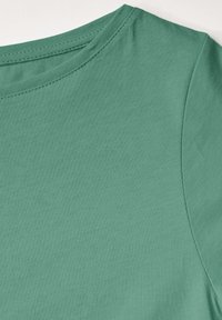 Kurzärmliges, rundhalsiges Oberteil in einer einfarbigen, gedeckten grünen Farbe. Hergestellt aus weichem Baumwollmaterial. Verfügt über eine glatte Textur und dezente Nähte.