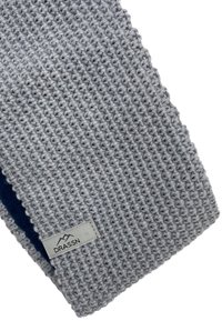 Gray knitted scarf with a textured pattern, featuring a navy blue interior and a small label with the brand name "DRASSN."