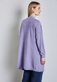 Ljuslila tröja med långa ärmar, avslappnad passform, ribbade ärmslut och detalj på ryggen. Kombinerad med mörkblå jeans, visas från baksidan.