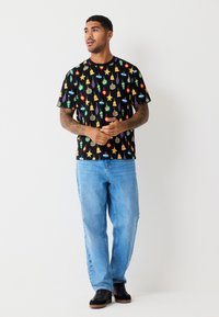 Sort T-shirt med korte ærmer med farverige feriedekorationer, kombineret med lyseblå jeans og sorte sko. Afslappet pasform og design.