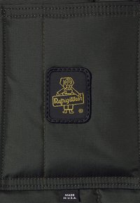 Svart tyg med en strukturerad yta som pryds av en gul tecknad hundlogotyp som håller i ett skylt med texten "RefrigiWear". Vit etikett med texten "Made in U.S.A."