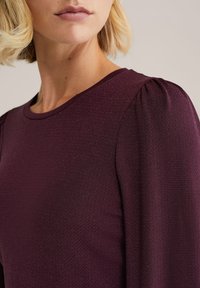 Burgundské textúrované tričko s okrúhlym výstrihom a jemne nariasenými rukávmi, s tkaným vzorom pre zvýšenie vizuálneho detailu.