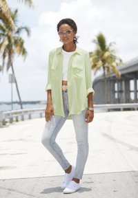 Light green button-up shirt over a white crop top, paired with light blue jeans and white sneakers. Pale sunglasses and a bracelet accent.
