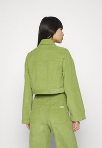 Chaqueta de pana recortada en un vibrante verde, con collar y mangas largas, presenta una textura acanalada y un detalle en el yugo trasero.