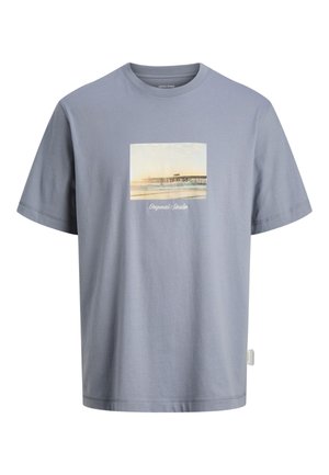 Lichtblauw T-shirt met korte mouwen met een foto van een kustpier en de tekst "Originals Studio" gedrukt op de voorkant.