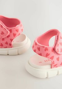 Rosa sandaler med hjärt-mönster, gummisulor och kardborreband. Vita texturerade fotbäddar ger dämpning och stabilitet.