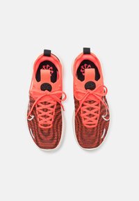 Scarpe da atletica rosse e nere con motivo a rete, dettagli bianchi e lacci piatti. Presentano un toggle circolare nero sul tallone.