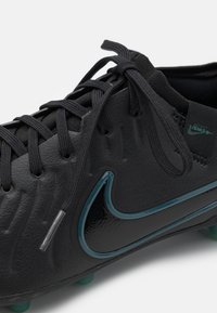 El botín de fútbol negro de Nike presenta un upper de cuero texturizado, acentos en teal, cordones estándar y tacos moldeados para tracción.
