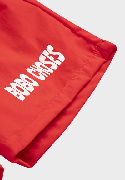 Tissu rouge avec une couture visible et un texte blanc imprimé en lettres majuscules stylisées affichant "BOBO CHOSES".