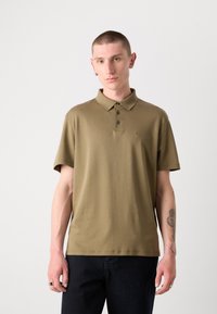 Polo olive en tissu doux, avec un col, une patte de boutonnage à trois boutons et un logo discret sur la poitrine. Manches courtes.