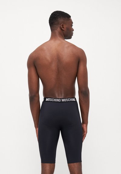 Shorts noirs mi-longs avec une ceinture en logo "Moschino" blanche, en tissu lisse et au design ajusté, présentés de dos sans détails supplémentaires.