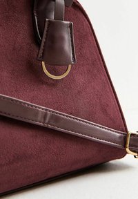 Borsa in suede bordeaux con tracolla in pelle marrone, hardware in anelli dorati e design strutturato con una superficie testurizzata.