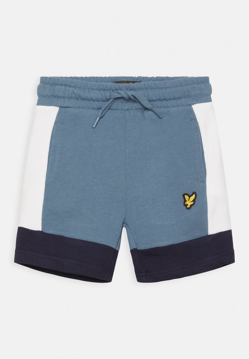 Short bleu avec panneaux latéraux blancs et ourlets bleu foncé, taille élastique avec cordon de serrage, et logo d’oiseau jaune sur la jambe gauche.