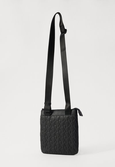 Sac bandoulière noir en matériau texturé, avec un motif géométrique, une bandoulière réglable et une fermeture zippée sur le dessus.