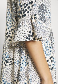 Šaty s květinovým vzorem v námořnické modři, modré a krémové barvě. Volánkové krátké rukávy a vrstvená sukně dodávají texturu a detaily.