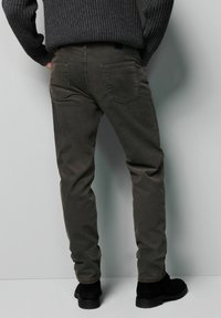 Bawełniane spodnie chinos w ciemnym oliwkowym odcieniu zieleni, z pięciokieszeniowym fasonem, widocznym przeszyciem i lekko zwężanym krojem. Noszone z czarnymi botkami za kostkę.