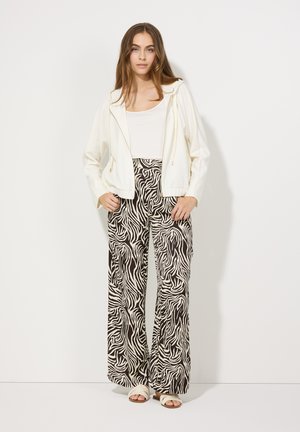 White zip-up hoodie paired with black and white zebra print wide-leg pants. The outfit features a round-neck white top and light sandals.