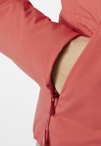 Rote wasserdichte Jacke mit weicher Textur, ausgestattet mit einer zipfelnden Tasche an der Seite und feinen Nähten entlang des Ärmels.