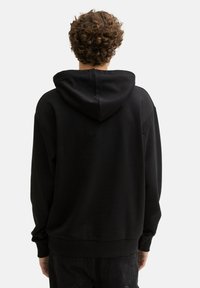 Felpa nera con tasca a marsupio, cappuccio con coulisse e polsini a costine. Il tessuto appare morbido e dalla texture liscia. Il modello è visto di spalle.