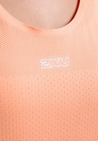 Leichtes Sportoberteil in Pfirsich mit einem strukturierten, atmungsaktiven Stoff. Mit Rundhalsausschnitt und einem weißen "2XU"-Logo auf der Brust.