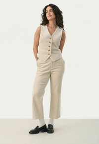 Beige corduroy vest met vijf gouden knopen, gecombineerd met bijpassende losse broek. Zwarte schoenen en grijze sokken maken de outfit compleet.
