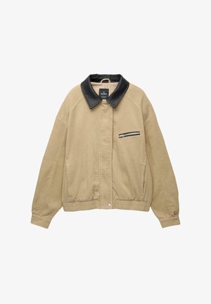 Beige kordfløjljakke med en sort læderkrave, frontlomme med lynlås, elastisk bund og lange ærmer. Simpel og struktureret design.