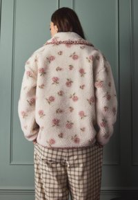 Fleecejakke i kremfarvet med pink blomsterbroderi, struktureret overflade, oversized pasform og flæsekant. Sammen med ternede bukser.