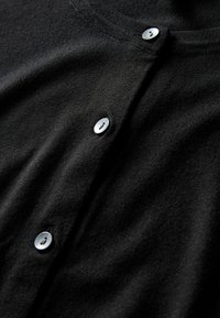 Černý svetr s kulatým výstřihem, vyrobený z hladkého materiálu, s pěti šedými knoflíky vpředu. Jemná textura a minimalistický design.