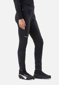 Pantaloni sportivi neri con dettagli trapuntati, tasche con zip e vestibilità aderente. Abbinati a calzature nere aderenti con dettagli bianchi.