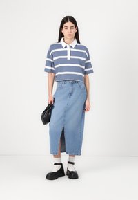 Camisa polo curta em azul com riscas brancas, combinada com uma saia de ganga de cintura alta com uma abertura frontal. Mala preta e sapatos de plataforma.