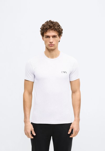 Balta īsroku kokvilnas T-krekls ar apaļu kakla izgriezumu; uz kreisās krūšu daļas neliels logotips. Gluda tekstūra.