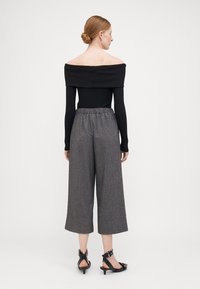 Off-shoulder svart ribbet topp i kombinasjon med grå vide bukser med elastisk liv, glatt tekstur og sorte hæler.