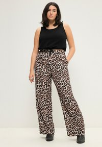 Schwarzes ärmelloses Top kombiniert mit weiten Leoparden-Print-Hosen in Beige, Braun und Schwarz, die über seitliche Taschen und einen lockeren Schnitt verfügen.