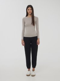 Top beige a maniche lunghe abbinato a pantaloni sportivi neri a gamba affusolata e sneakers bianche. Il top ha un collo rotondo; i pantaloni presentano polsini elastici.
