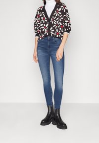 Black and white floral cardigan with red accents, paired with blue skinny jeans and black ankle boots with chunky soles.