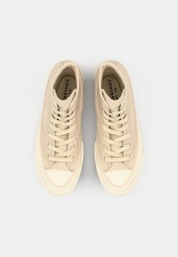 Høye beige kanvas sneakers med en jevn tekstur, rund tåhette og seks øyelets snøring. Stempel med logo på tungen.