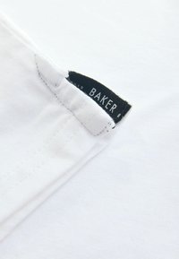 Bílé bavlněné tričko s hladkou texturou. Na švu u krku má černou etiketu s bílým nápisem „BAKER“. Jednoduchý design.